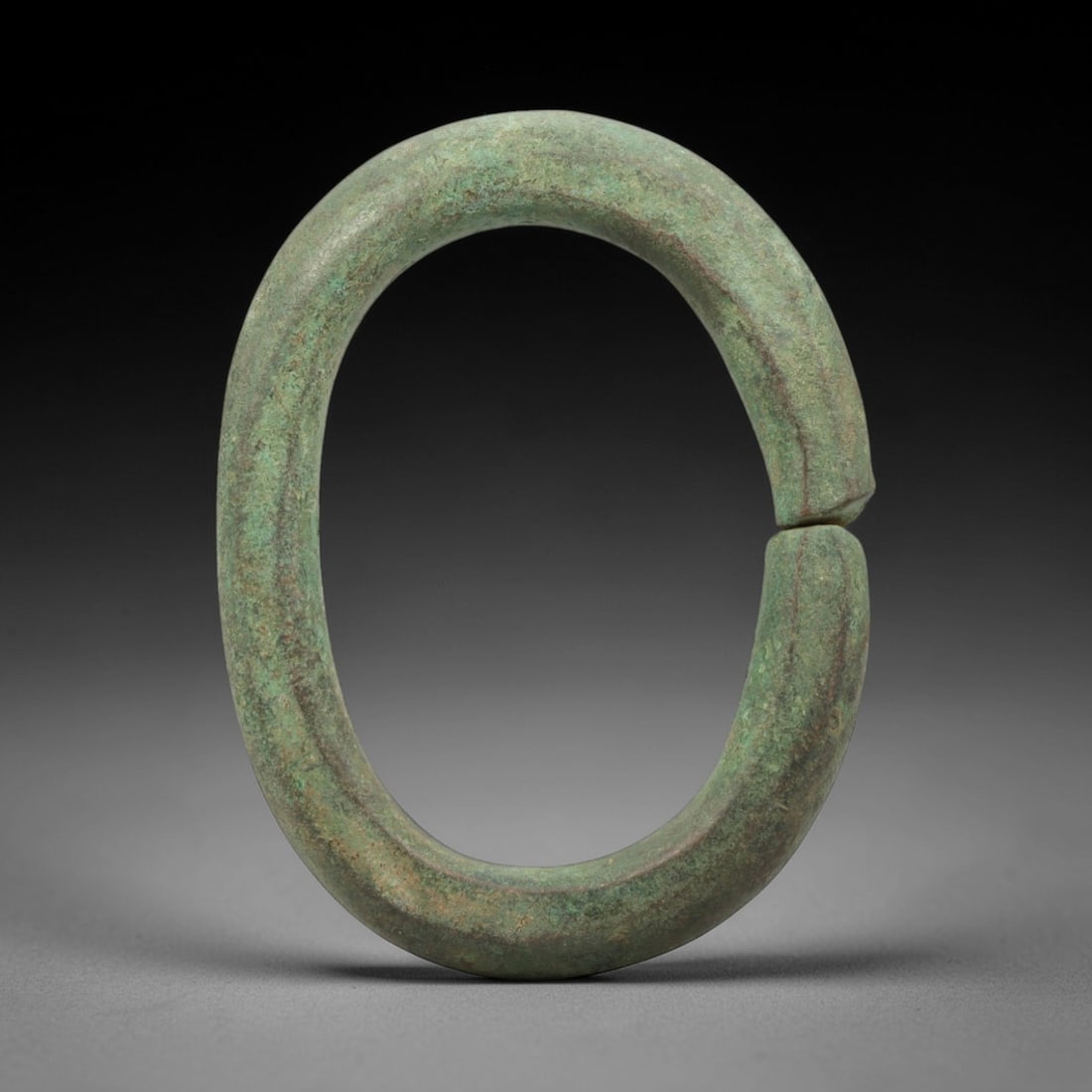 A Roman Bronze Bracelet, 1st-3rd Century CE, 1FV: Cast from bronze with a thick, rounded section, the bracelet is formed as a near-complete circle with a narrow terminal gap. The surface is covered in a uniform green patina with subtle linear striati