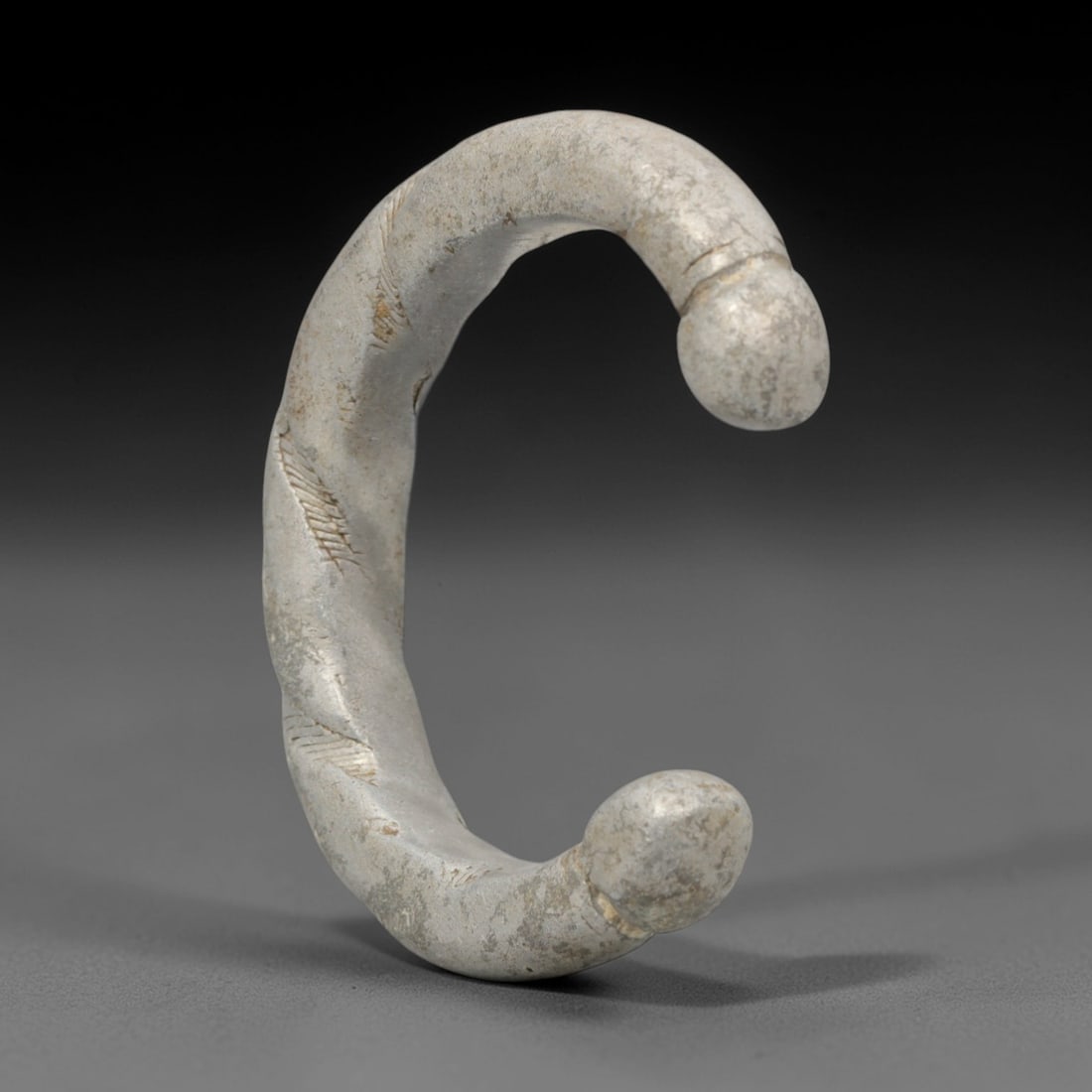An African Silvered Aluminium Bracelet, 20th Century, 90FT: Formed from silvered aluminium, the bracelet is constructed as an open C-shape with a twisted, spiraled body and rounded, bulbous terminals. The surface is decorated with incised linear striations fol