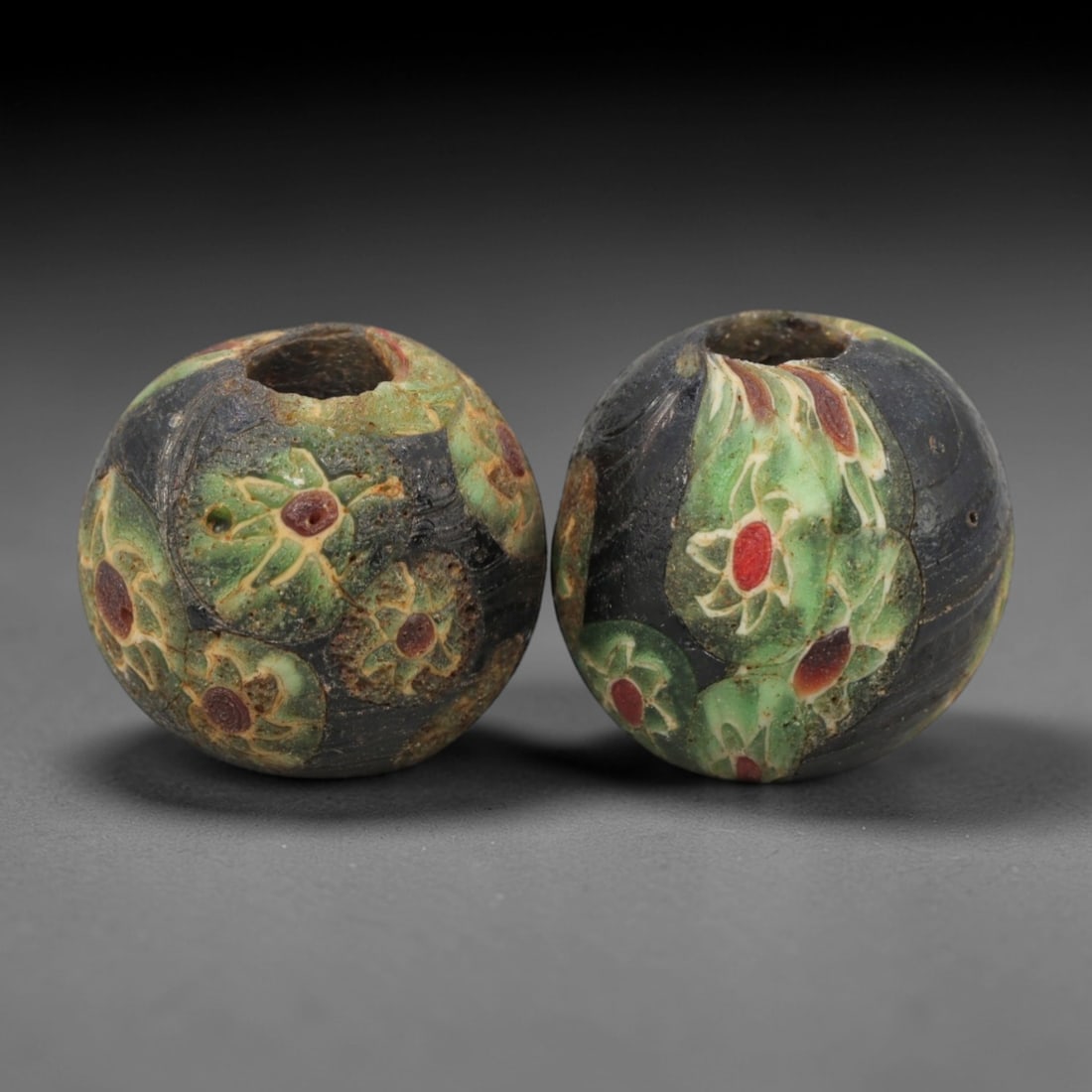 A Pair of Venetian Millefiori Glass Beads, 19th-20th Century, 66AD: Fabricated from opaque black glass, each bead is formed as a sphere with a central drilled perforation. The surface is decorated with characteristic millefiori canes, featuring circular floral motifs