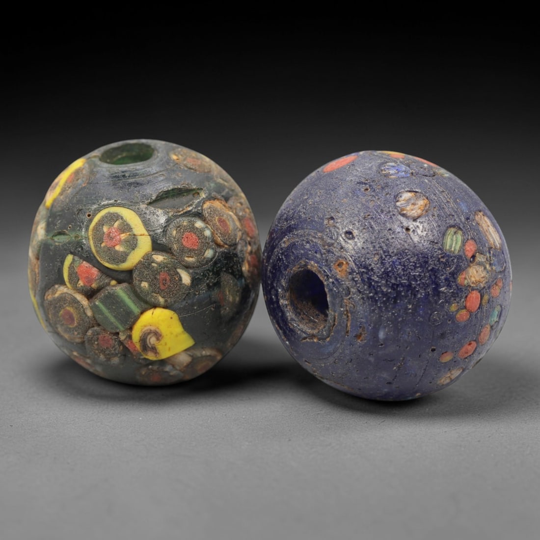 A Pair of Venetian Glass Trade Beads, 19th-20th Century, 19ZM: Formed as spherical beads, each is crafted from translucent glass with a central perforation for suspension. The surface is decorated with multiple polychrome eye and floral motifs, featuring red, yel