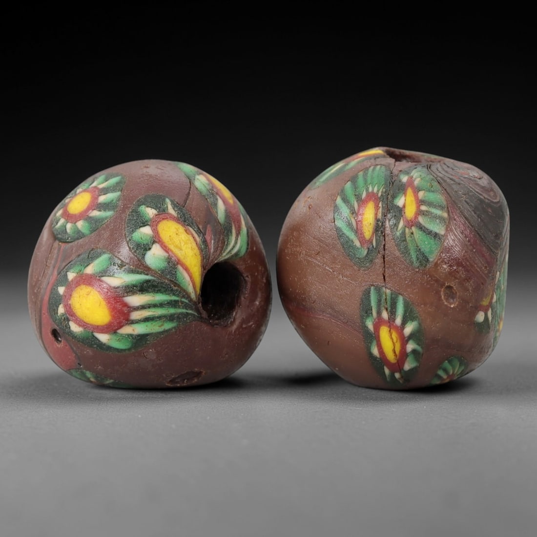 A Pair of Venetian Glass Trade Beads, 19th-20th Century, 69ZM: Formed as spherical beads, each is crafted from opaque reddish-brown glass with a central perforation for suspension. The surface is decorated with multiple polychrome eye motifs, each featuring a yel