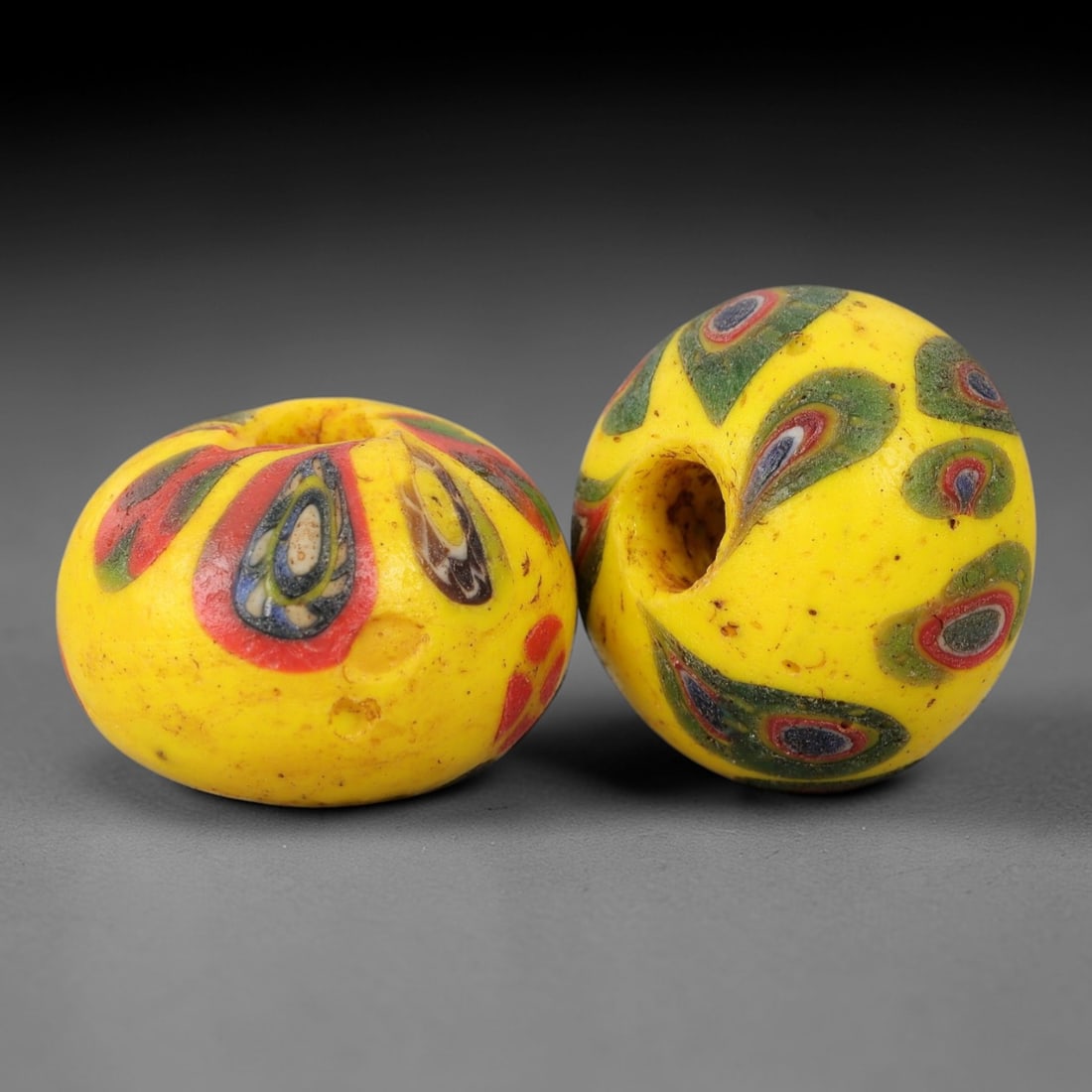 A Pair of Venetian Glass Trade Beads, 19th-20th Century, 75ZM: Formed as spherical beads, each is crafted from opaque yellow glass with a central perforation for suspension. The surface is decorated with multiple polychrome eye motifs, each featuring a dark core,