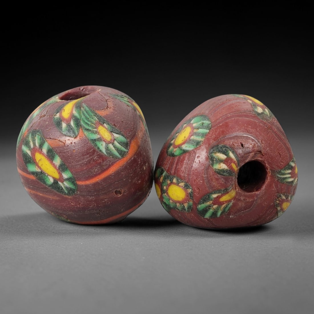 A Pair of Venetian Glass Trade Beads, 19th-20th Century, 63ZM: Formed as ovoid beads, each is crafted from opaque reddish-brown glass with a central perforation for suspension. The surface is decorated with multiple polychrome eye motifs, each featuring a yellow