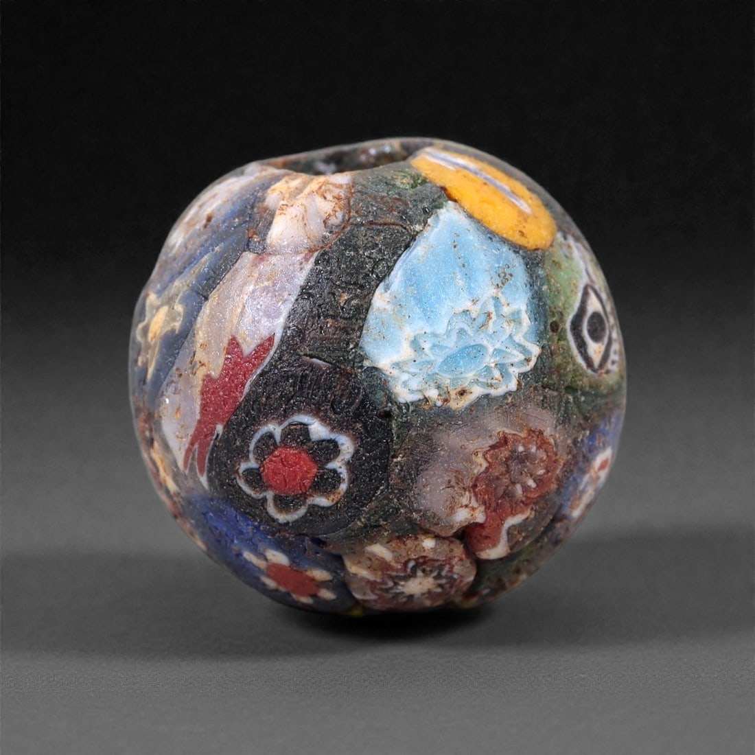 Antique Glass Bead - Venetian Scramble Cane Sphere, 13Z: This spherical glass bead is formed from a dark glass body incorporating a dense assemblage of scrambled millefiori and patterned cane fragments, fused into the surface using the Venetian "scramble" o