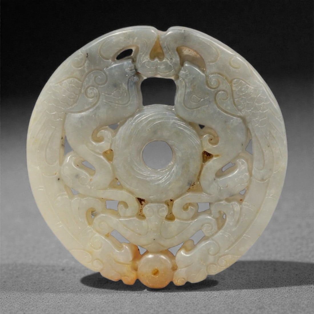 A Chinese Archaistic Jade Openwork Disc, 20th Century, 35YC: The disc is carved from pale celadon jade with areas of honey and russet coloration, the stone showing soft translucency and natural inclusions. It is worked as a circular plaque with a central perfor