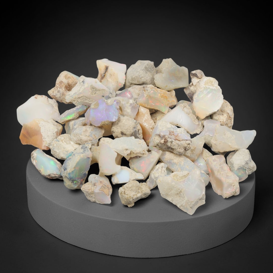 An Ethiopian Welo Opal Rough Lot, 47.67g, 55ZH: A parcel of rough Welo opal, with individual pieces ranging from 1-2.5 cm in size. The specimens exhibit a milky to translucent base, with visible play-of-color displaying flashes of blue, green, yell