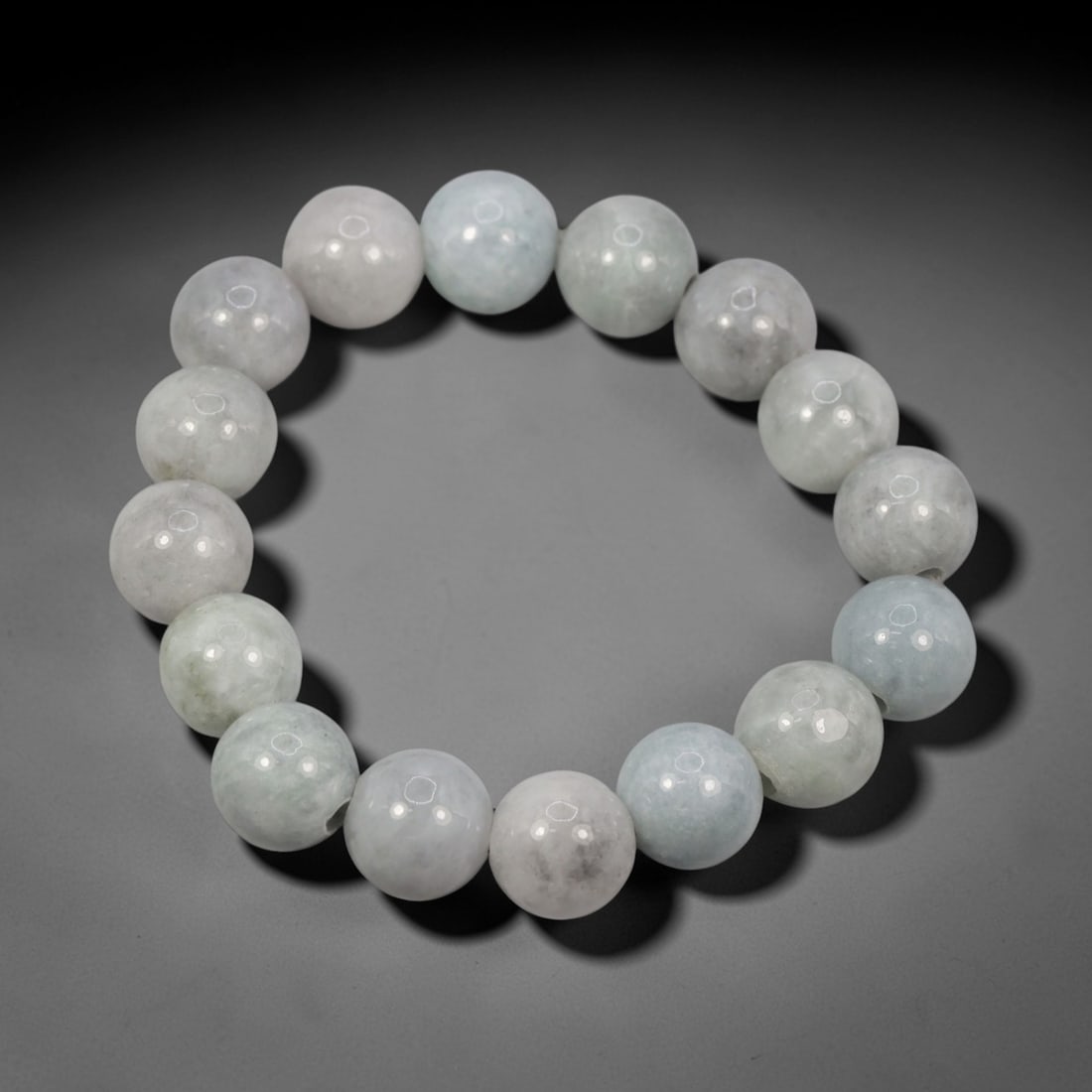A Chinese Jadeite Jade Bead Bracelet, 20th Century, 72FS: Composed of spherical beads of pale white and celadon jadeite jade with natural veining and minor internal inclusions, the bracelet is strung in a continuous loop. The beads exhibit a smooth, polished