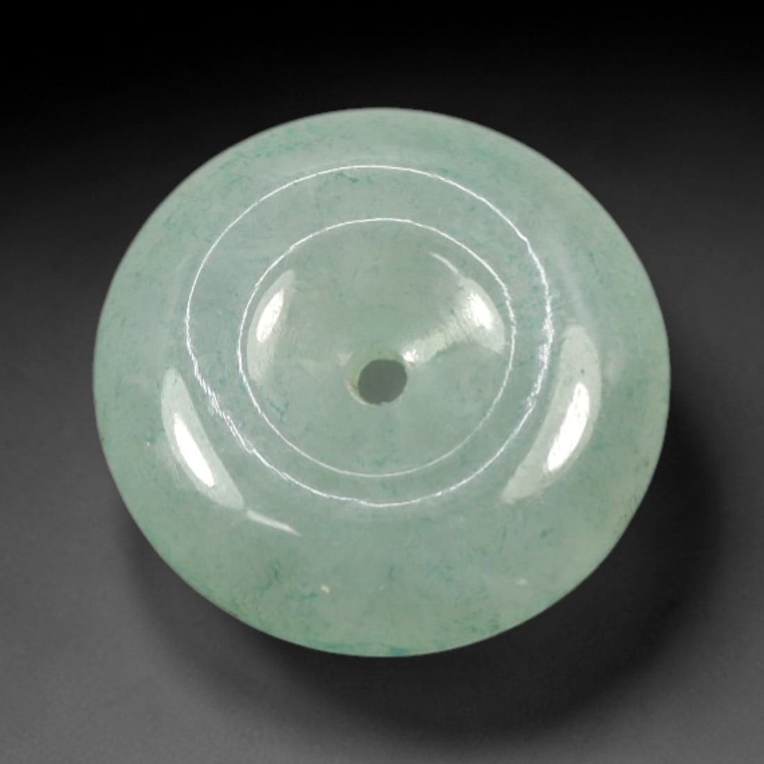 A Chinese Jadeite Jade Bead, 20th Century, 8XN: Carved from pale green jadeite jade with subtle tonal variation and minor natural inclusions, the bead is formed as a spherical object with a smooth, highly polished surface. The form features a centr