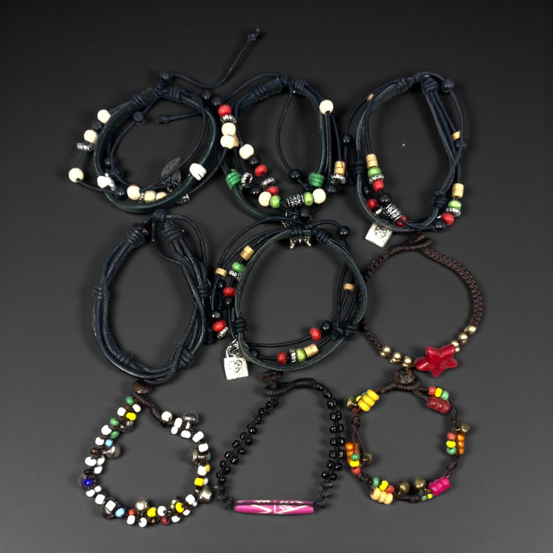 A Group of Nine Leather and Beaded Bracelets, Late 20th-Early 21st Century, 36ZG: The group comprises nine bracelets constructed primarily from dark-toned leather cords combined with assorted beads and minor metal fittings. The designs vary and include wrapped and layered leather e