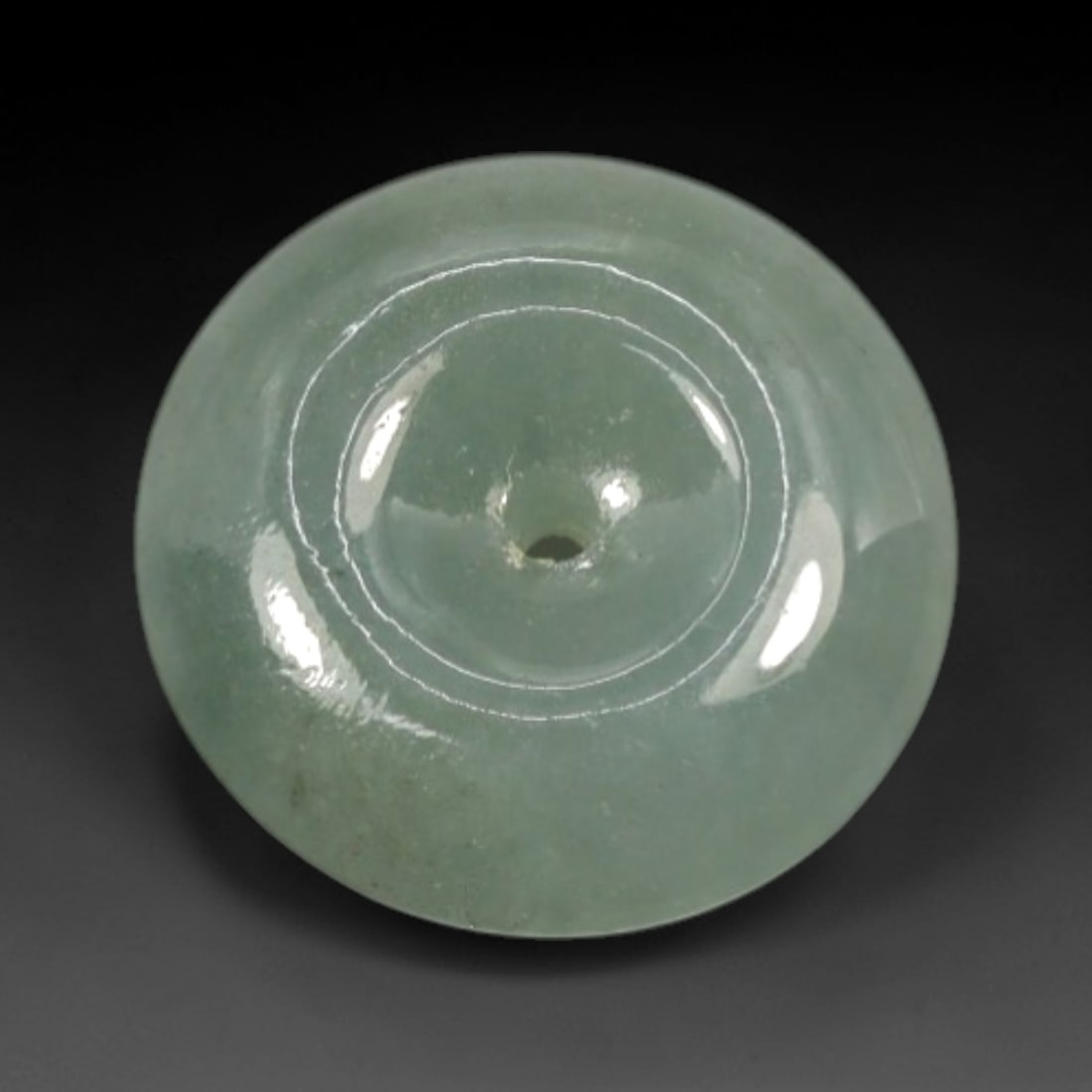 A Chinese Jadeite Jade Bead, 20th Century, 5XN: Carved from pale green jadeite jade with subtle tonal variation and minor natural inclusions, the bead is formed as a spherical object with a smooth, highly polished surface. The form features a centr