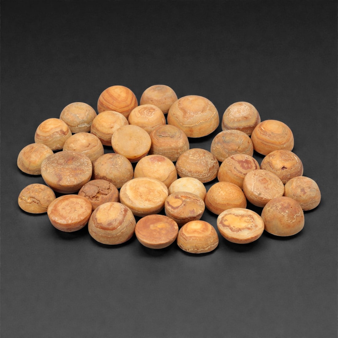 A Group of Tibetan Agate Luk Mik ("Goat's Eye") Beads, 19th-20th Century, 49FK: Comprising thirty-four agate beads carved from banded chalcedony, each bead formed in a hemispherical to lentoid shape with rounded domed upper surfaces and flattened bases, displaying naturally occur
