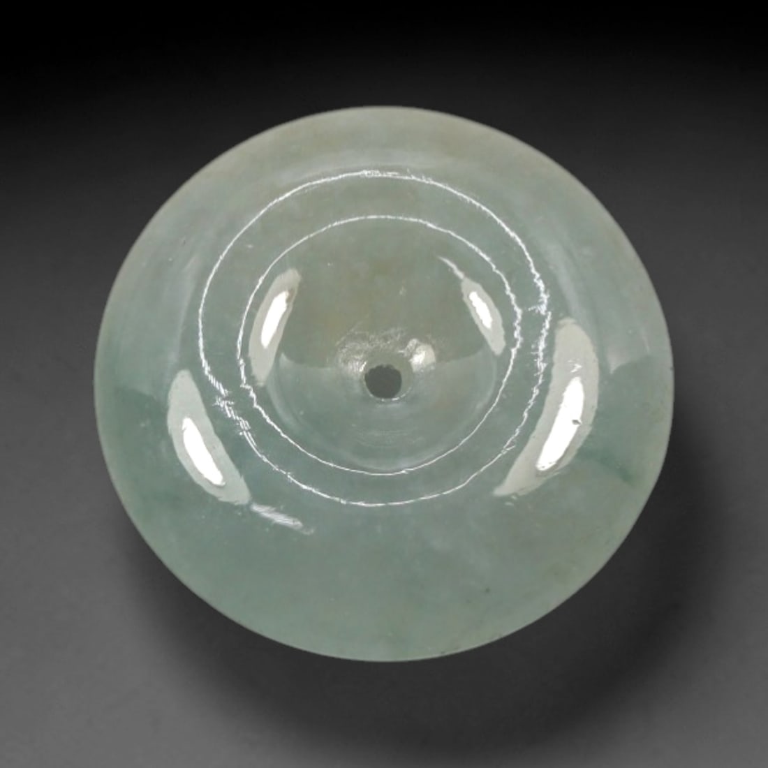 A Chinese Jadeite Jade Bead, 20th Century, 24XN: Carved from pale green jadeite jade with subtle tonal variation and minor natural inclusions, the bead is formed as a spherical object with a smooth, highly polished surface. The form features a centr