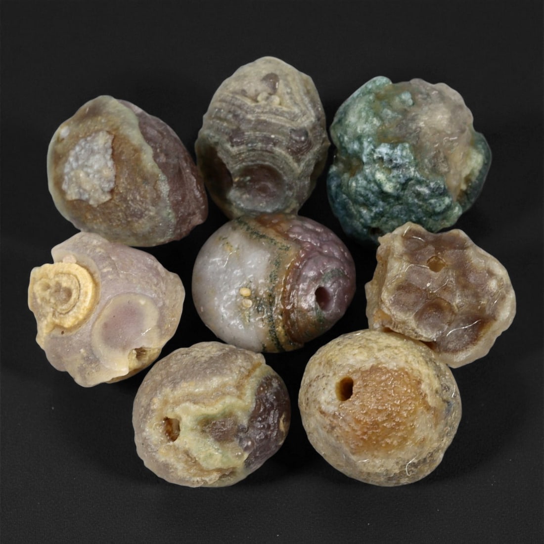 A Group of Mongolian Agate Eye Beads, 20th Century, 99FS: The group consists of eight beads, formed from agate displaying prominent natural concentric banding and distinct eye-like formations. The specimens exhibit a palette of green, lavender, tan, and tran