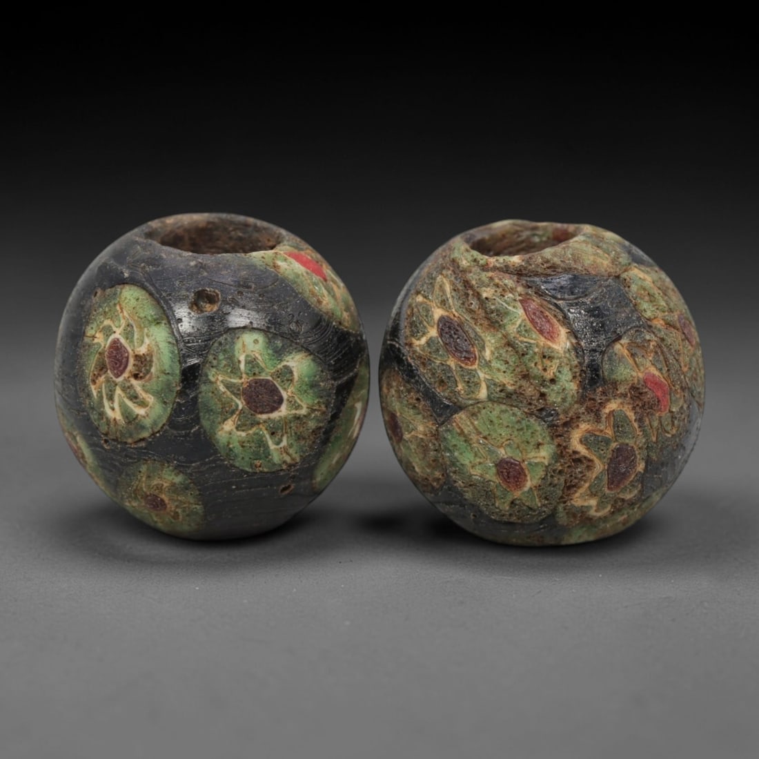 A Pair of Venetian Millefiori Glass Beads, 19th-20th Century, 76AD: Fabricated from opaque black glass, each bead is formed as a sphere with a central drilled perforation. The surface is decorated with characteristic millefiori canes, featuring circular floral motifs