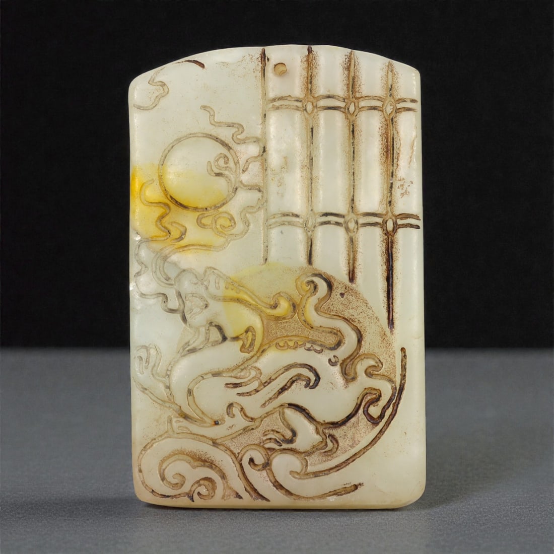 A Chinese Jade Dragon and Sun Relief Plaque, 20th Century, 45YA: Carved from pale white jade with areas of warm russet and yellowish staining following the natural inclusions of the stone, the plaque is rectangular in form with a flat reverse and softly rounded edg