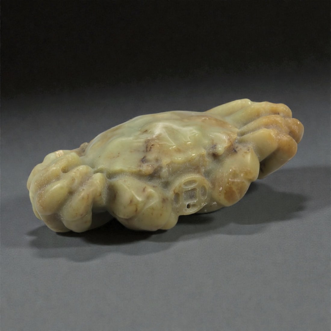 A Chinese Nephrite Jade Crab, 20th Century, 90FB: Carved from mottled pale green to yellow-brown nephrite jade with natural inclusions and tonal variation, the figure is modeled as a crab shown with its body flattened and legs tucked beneath the cara