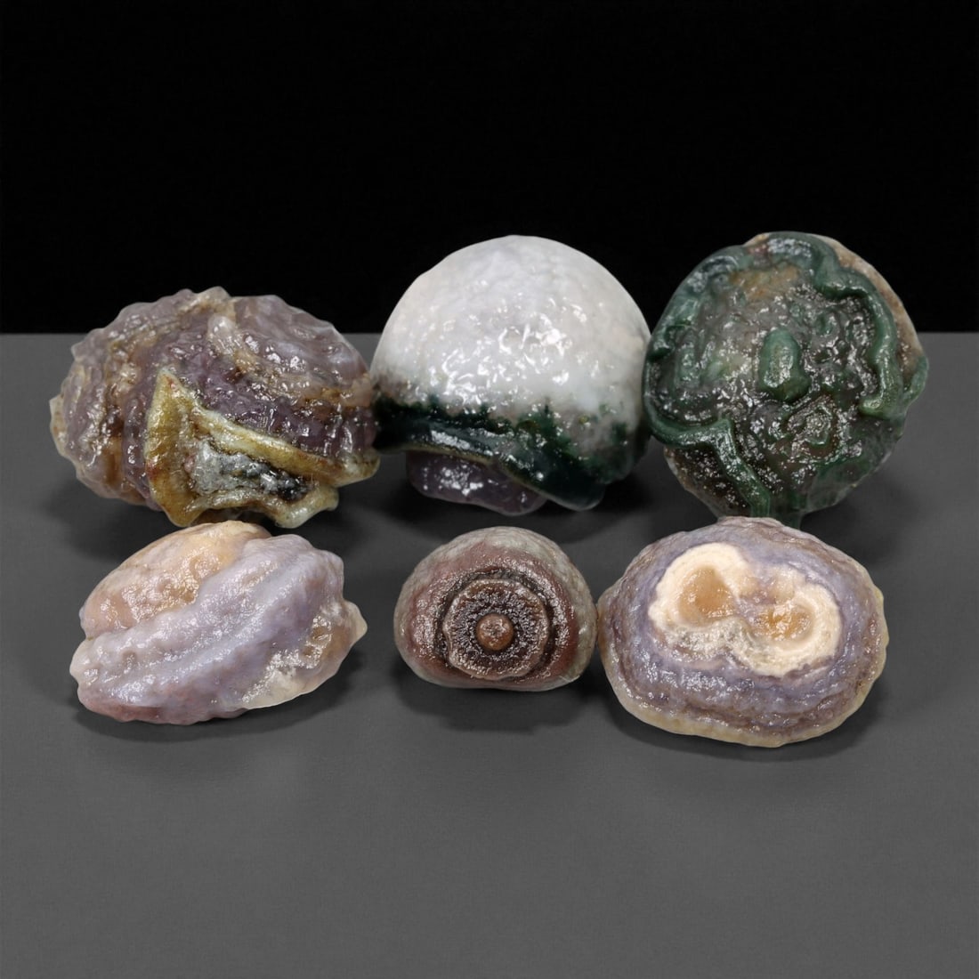 A Group of Mongolian Agate Eye Beads, 20th Century, 98FS: The group consists of six beads, formed from agate displaying prominent natural concentric banding and distinct eye-like formations. The specimens exhibit a palette of green, lavender, tan, white, and