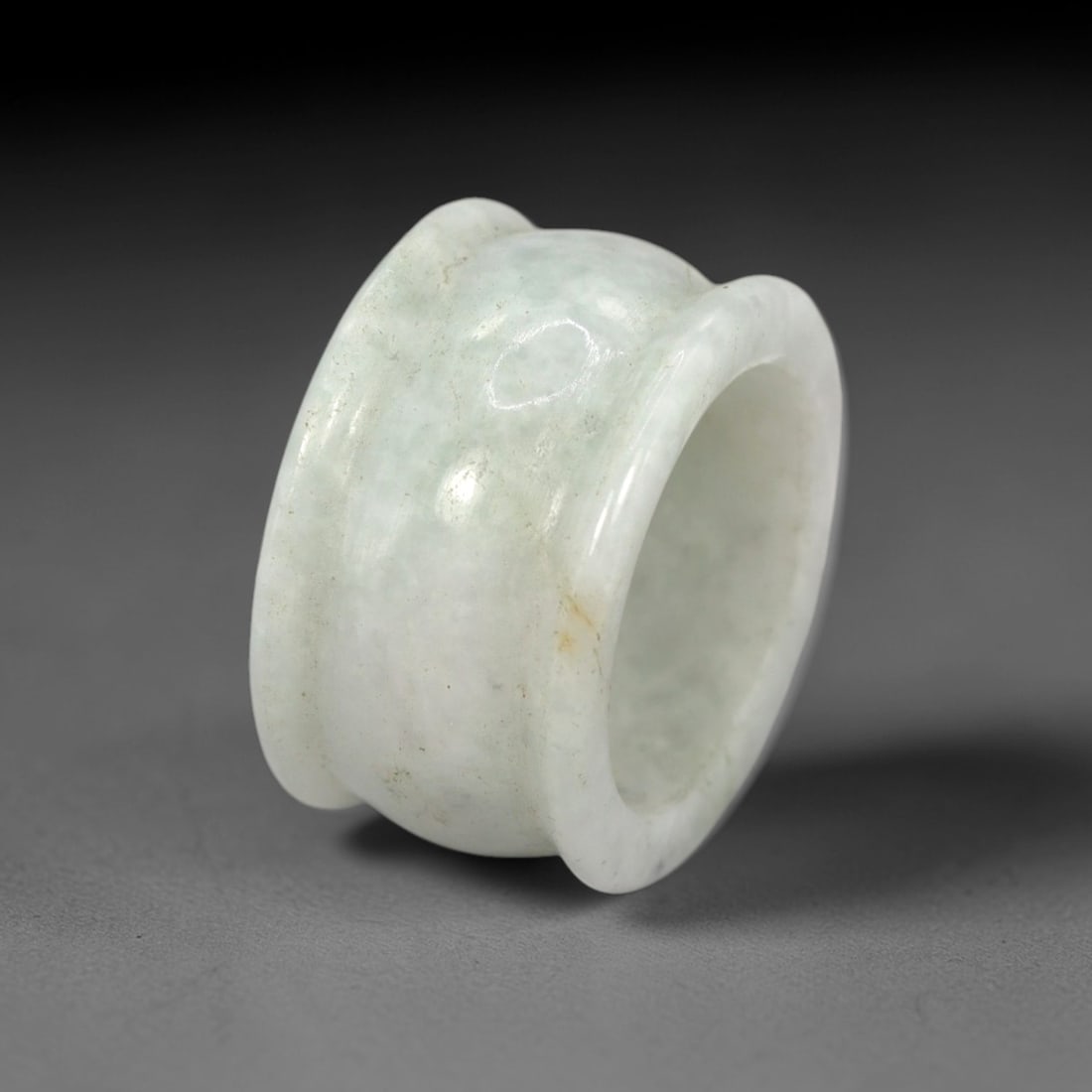 A Chinese Jadeite Jade Archer's Ring, 20th Century, 74FT: Carved from pale greenish-white jadeite jade with a smooth, highly polished surface, the ring is formed as a thick, cylindrical band with a slightly flared outer profile and a concave inner surface. T