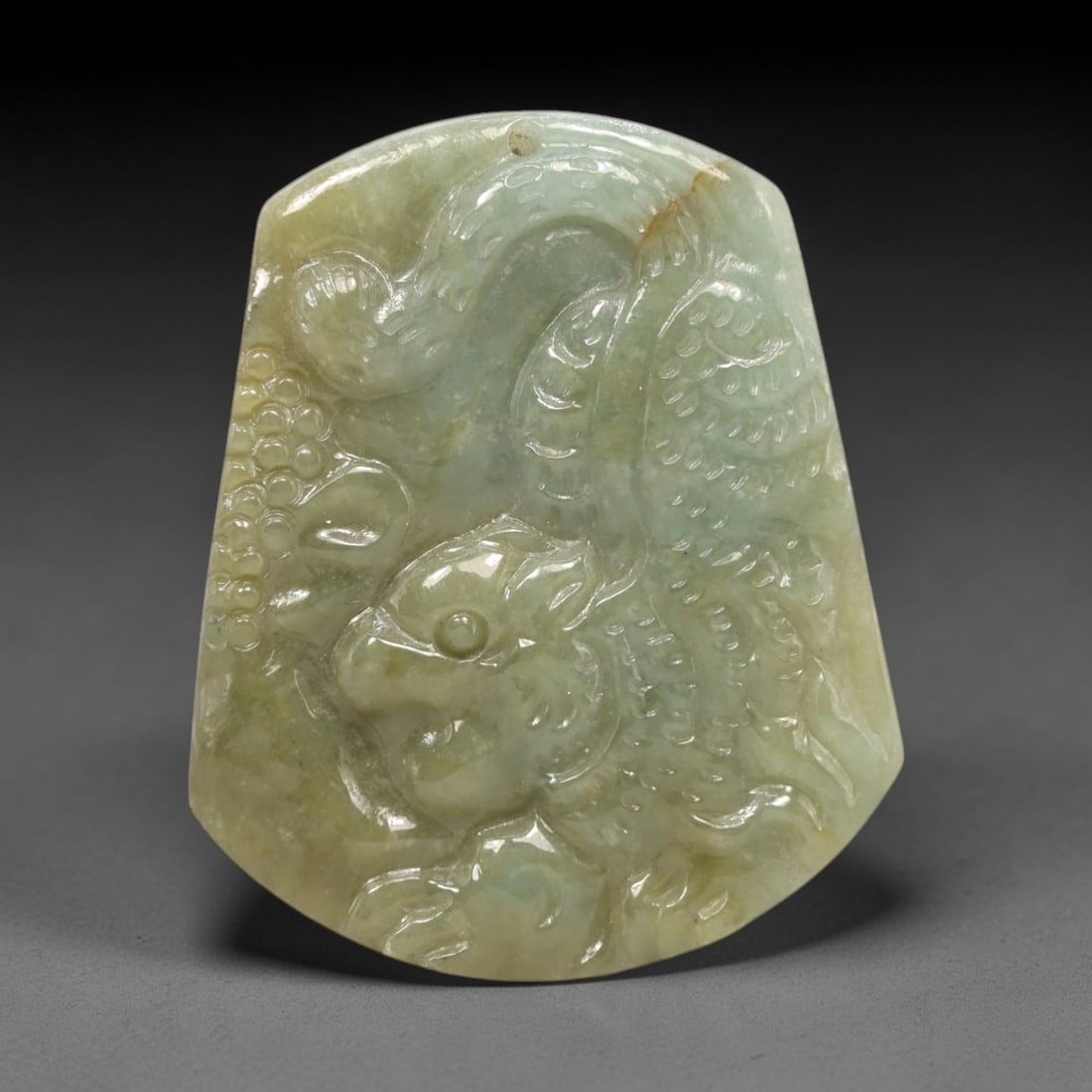 A Chinese Jadeite Jade Qilin Pendant, 20th Century, 24FR: Carved from pale greenish-yellow jadeite jade with natural tonal variation and a subtle russet inclusion, the pendant is shaped as a shield-like form with a top suspension hole. A qilin is rendered in
