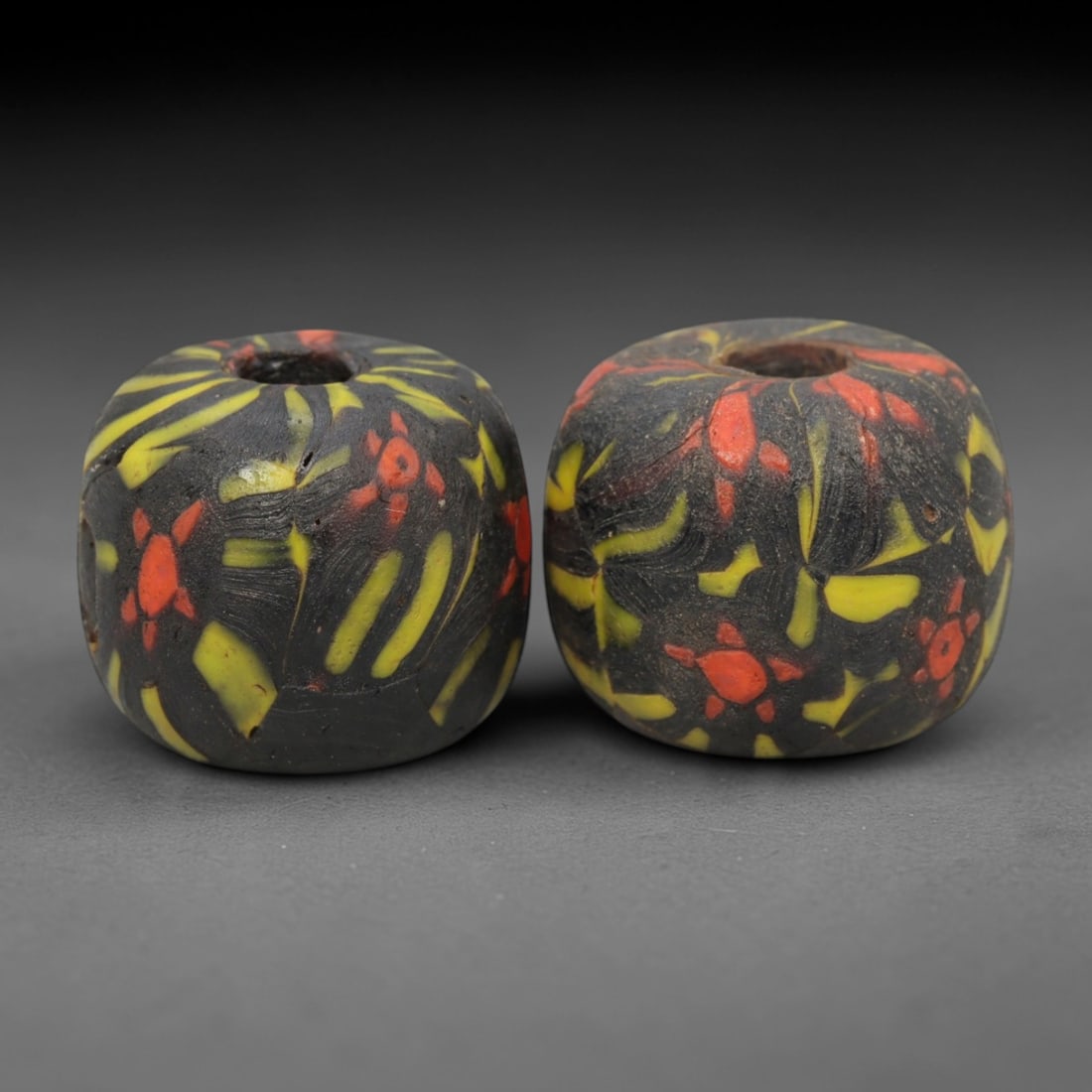 A Pair of Venetian Millefiori Glass Beads, 19th-20th Century, 47AD: Fabricated from opaque black glass, each bead is formed as a short cylinder with a central drilled perforation. The surface is decorated with characteristic millefiori canes, featuring elongated yello