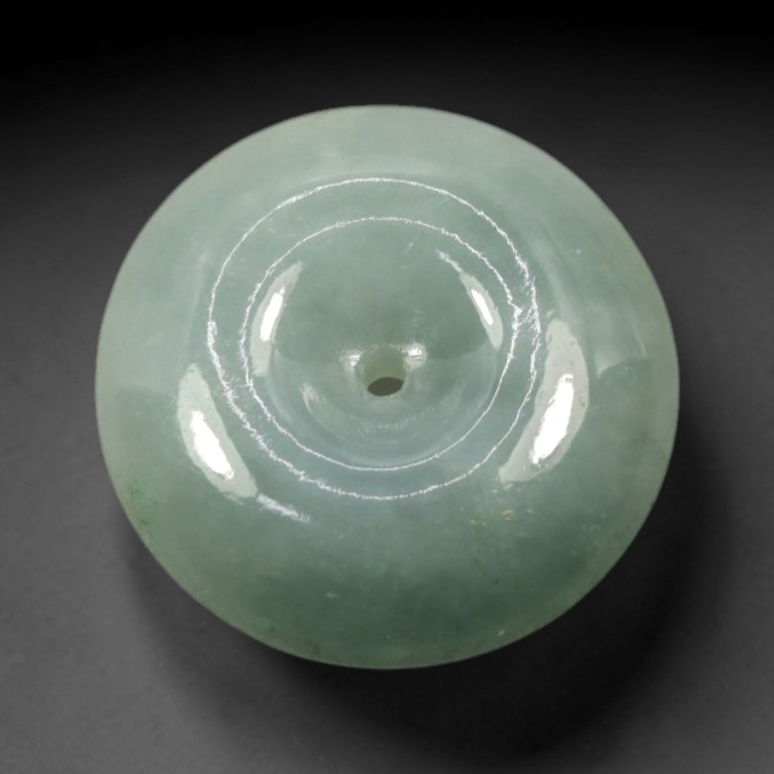 A Chinese Jadeite Jade Bead, 20th Century, 26XN: Carved from pale green jadeite jade with subtle tonal variation and minor natural inclusions, the bead is formed as a spherical object with a smooth, highly polished surface. The form features a centr