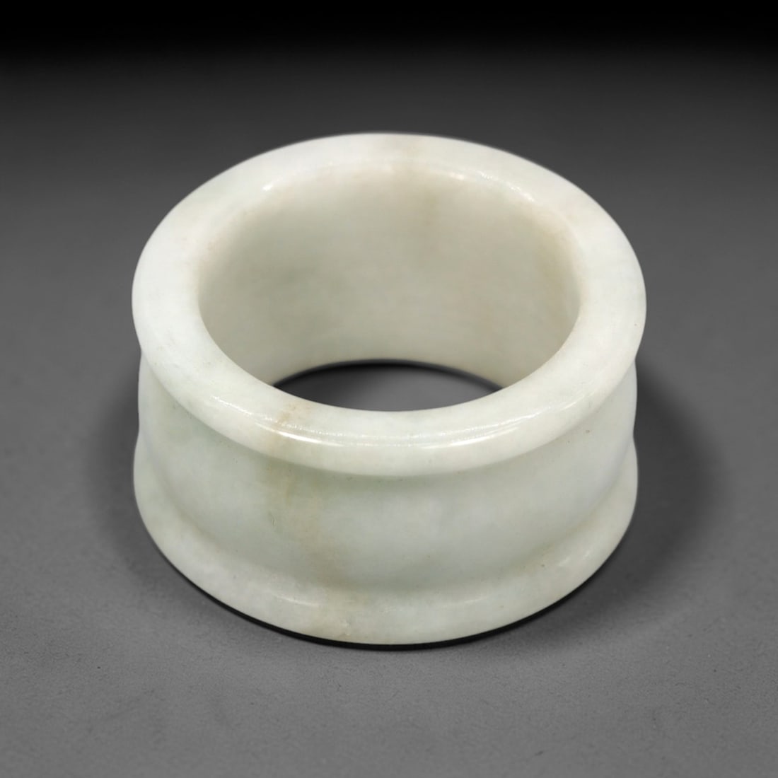 A Chinese Jadeite Jade Archer's Ring, 20th Century, 22FT: Carved from pale greenish-white jadeite jade with a smooth, highly polished surface, the ring is formed as a thick, cylindrical band with a slightly flared outer profile and a concave inner surface. T