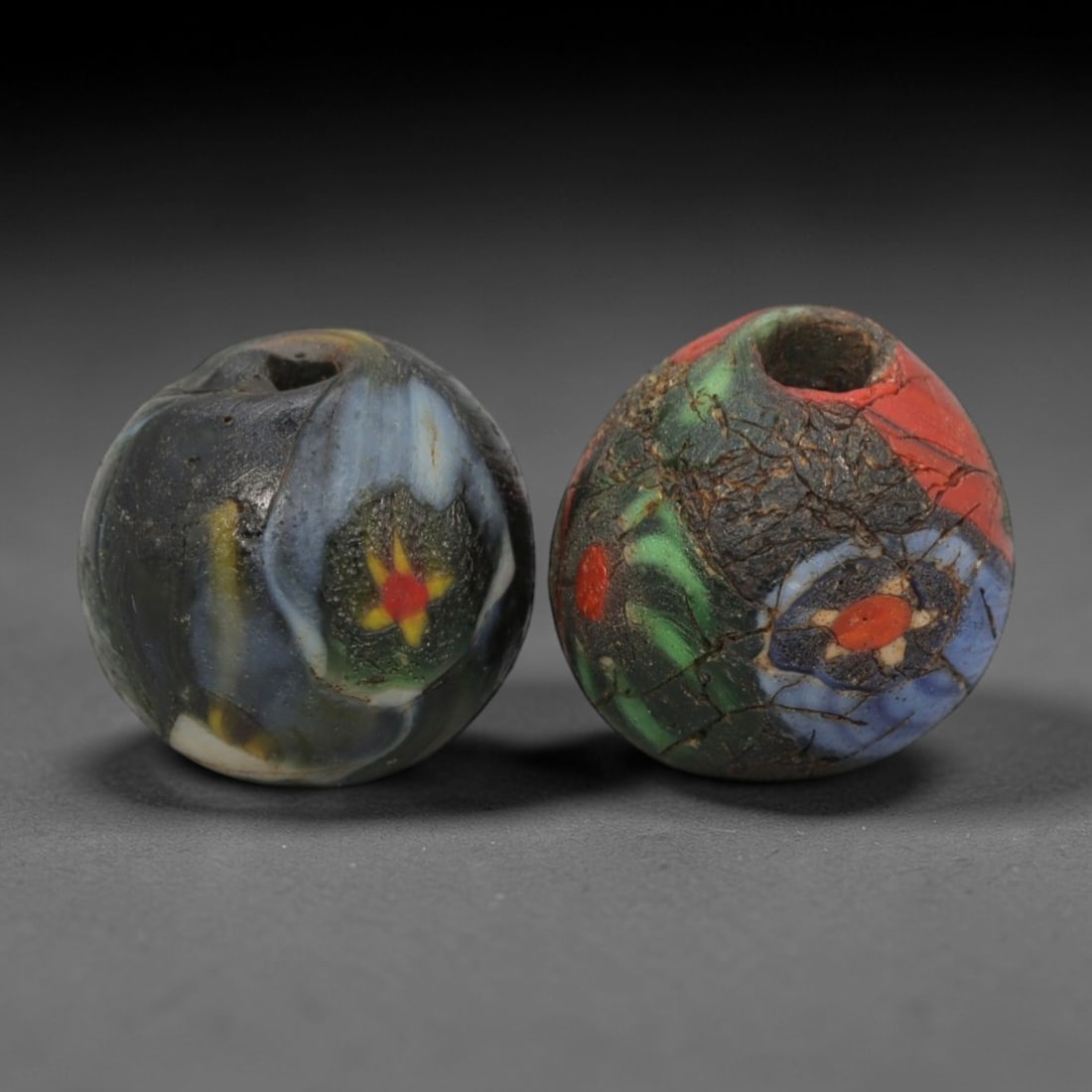 A Pair of Venetian Millefiori Glass Beads, 19th-20th Century, 51AD: Fabricated from translucent and opaque glass, each bead is formed as a sphere with a central drilled perforation. The surface is decorated with characteristic millefiori canes: one bead displays a flo