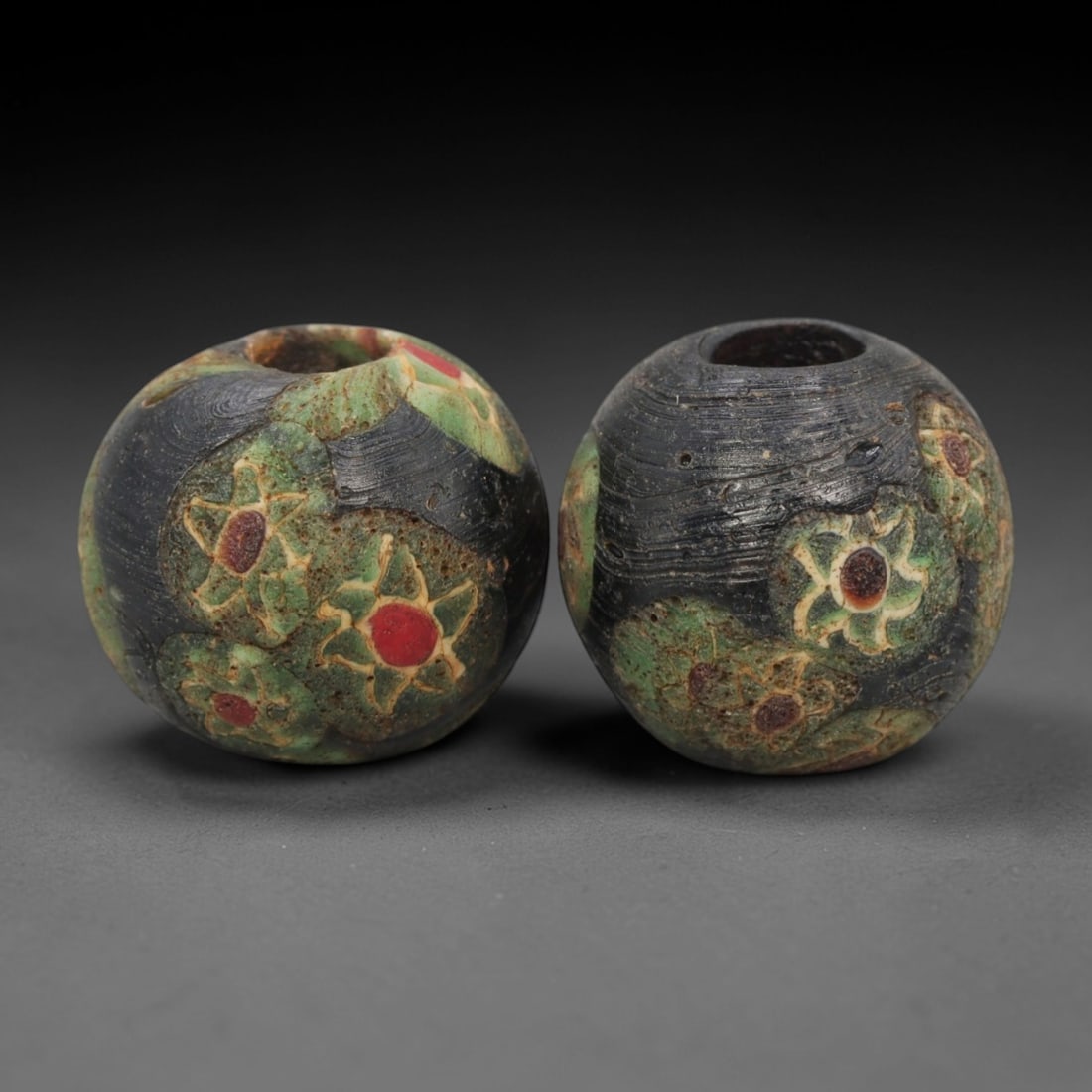 A Pair of Venetian Millefiori Glass Beads, 19th-20th Century, 55AD: Fabricated from opaque black glass, each bead is formed as a sphere with a central drilled perforation. The surface is decorated with characteristic millefiori canes, featuring circular floral motifs