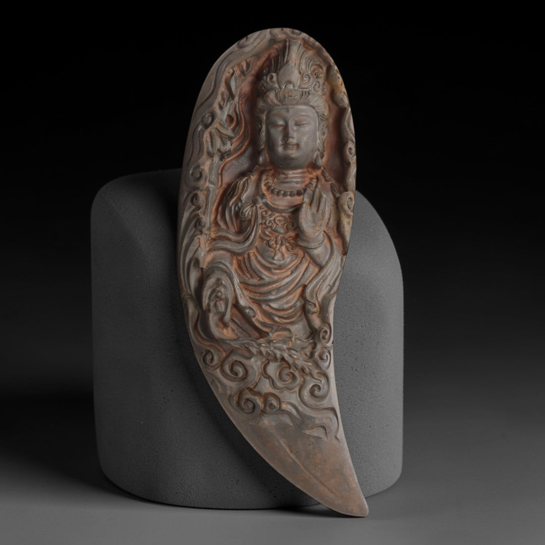 A Chinese Horn or Bone Guanyin Pendant Amulet, 20th Century, 80FV: Carved from horn or bone with a dark, aged patina and subtle tonal variations, the pendant is shaped like a stylized tusk or claw. The front face is deeply carved in high relief, depicting the bodhisa