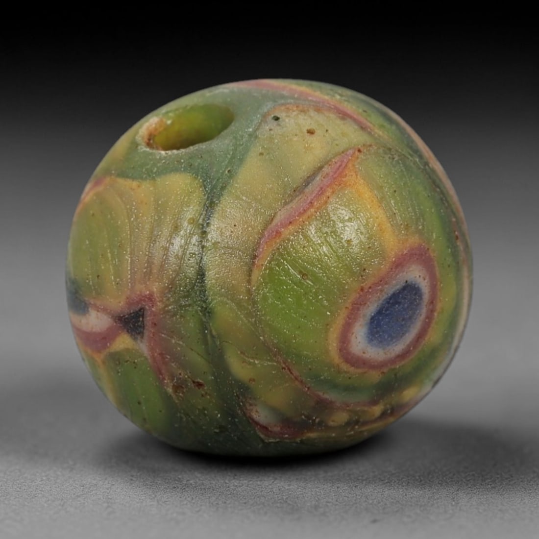 A Sino-Himalayan Glass Eye Bead, 18th-19th Century, 100FV: Formed from translucent green glass with swirling yellow and pale green filamentary inclusions characteristic of mosaic glass working, the bead is spherical with a central perforation for suspension.