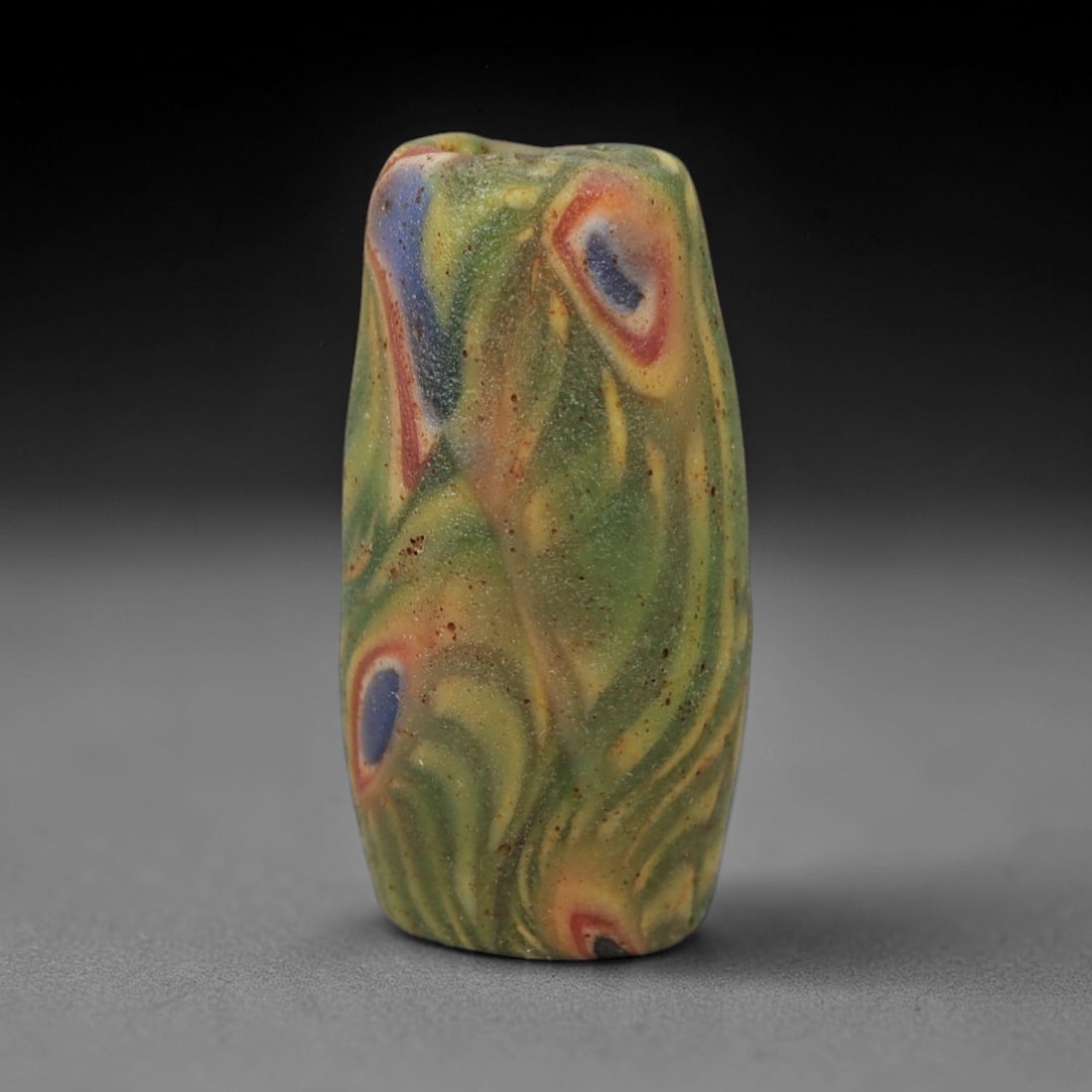 A Sino-Himalayan Glass Eye Bead, 18th-19th Century, 97FV: Formed from green glass with swirling yellow and pale green filamentary inclusions characteristic of mosaic glass working, the bead is cylindrical with a central perforation for suspension. The surfac