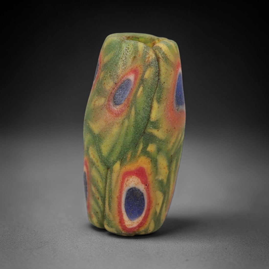 A Sino-Himalayan Glass Eye Bead, 18th-19th Century, 99FV: Formed from translucent green glass with swirling yellow and pale green filamentary inclusions characteristic of mosaic glass working, the bead is barrel-shaped with a central perforation for suspensi