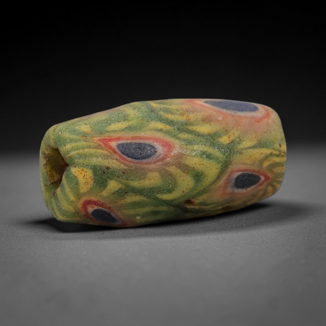 A Sino-Himalayan Glass Eye Bead, 18th-19th Century, 98FV: Formed from translucent green glass with swirling yellow and pale green filamentary inclusions characteristic of mosaic glass working, the bead is barrel-shaped with a central perforation for suspensi