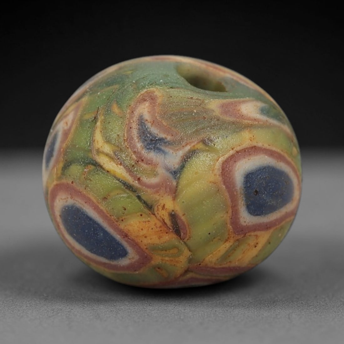 A Sino-Himalayan Glass Eye Bead, 18th-19th Century, 2FW: Formed from translucent green glass with swirling yellow and pale green filamentary inclusions characteristic of mosaic glass working, the bead is spherical with a central perforation for suspension.