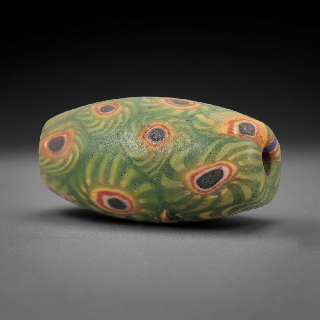 A Sino-Himalayan Glass Eye Bead, 18th-19th Century, 58FW: Formed from green glass with swirling yellow and pale green filamentary inclusions characteristic of mosaic glass working, the bead is barrel-shaped with a central perforation for suspension. The surf