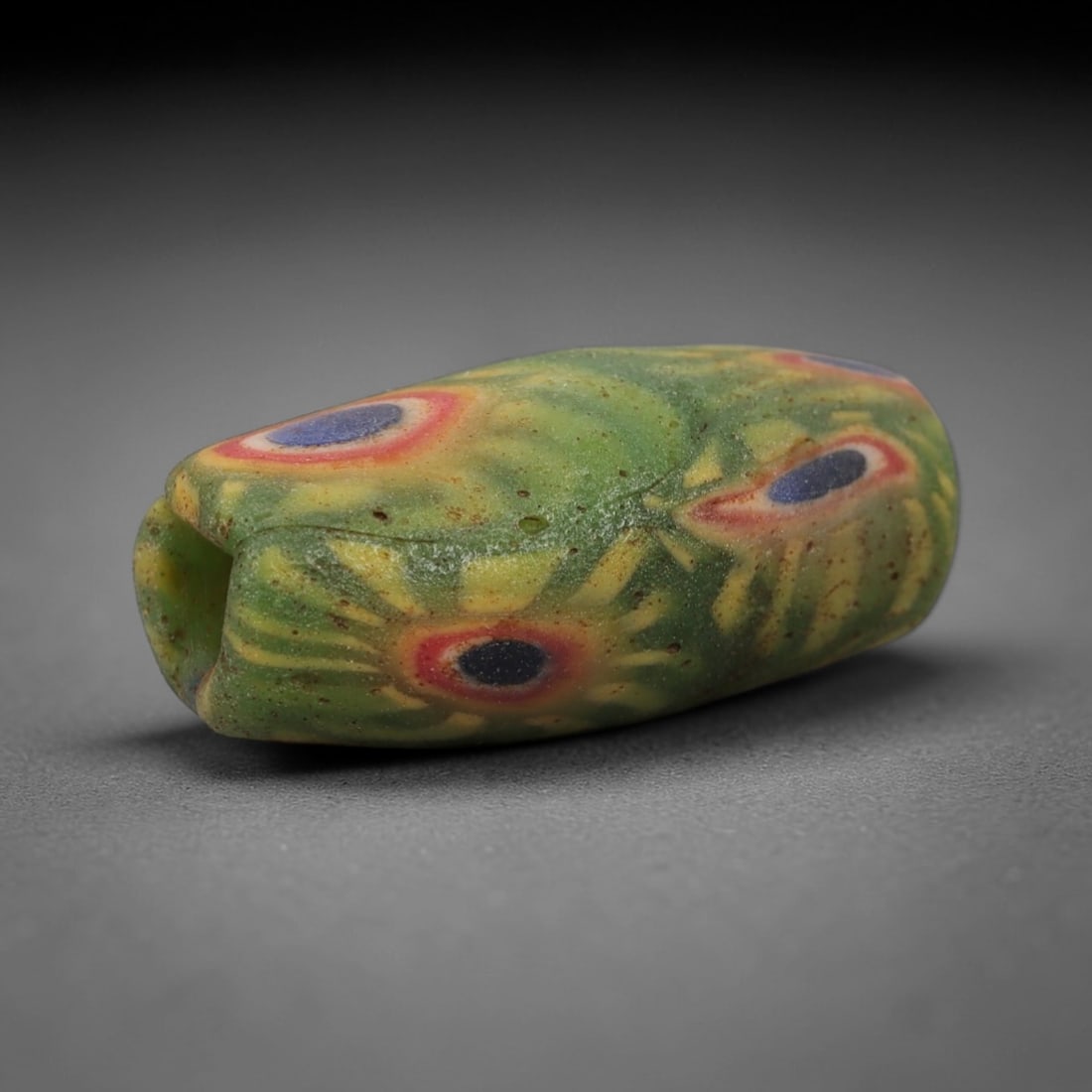 A Sino-Himalayan Glass Eye Bead, 18th-19th Century, 95FV: Formed from translucent green glass with swirling yellow and pale green filamentary inclusions characteristic of mosaic glass working, the bead is barrel-shaped with a central perforation for suspensi