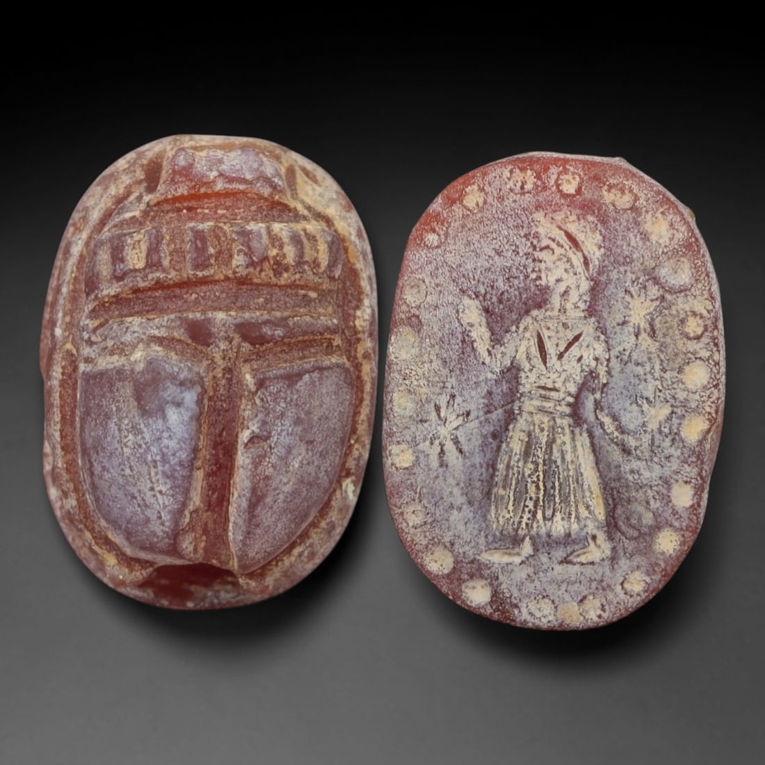 An Ancient Near Eastern Carnelian Scarab Stamp Seal, 1st Millennium BCE, 14ZM: Carved from translucent carnelian with a rich reddish-brown hue and natural surface patination, the object is formed as an oval scarab seal. The dorsal side is modeled in low relief with a segmented c