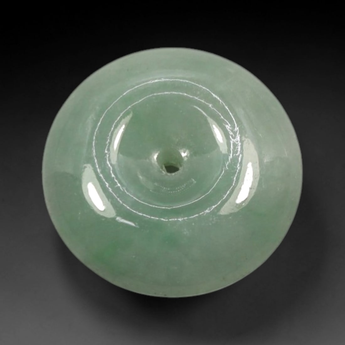 A Chinese Jadeite Jade Bead, 20th Century, 29XN: Carved from pale green jadeite jade with subtle tonal variation and minor natural inclusions, the bead is formed as a spherical object with a smooth, highly polished surface. The form features a centr