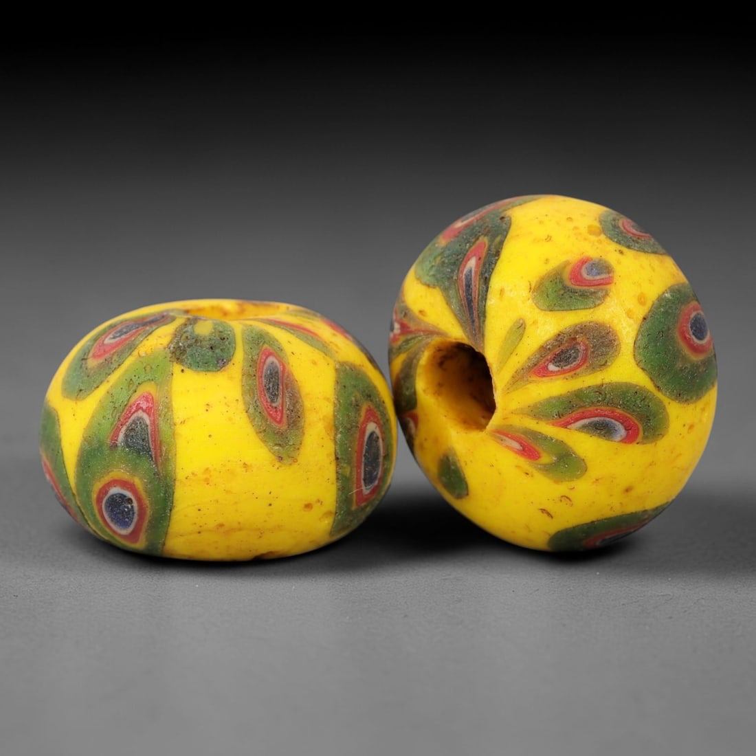 A Pair of Venetian Glass Trade Beads, 19th-20th Century, 62ZM: Formed as spherical beads, each is crafted from opaque yellow glass with a central perforation for suspension. The surface is decorated with multiple polychrome eye motifs, each featuring a dark core,