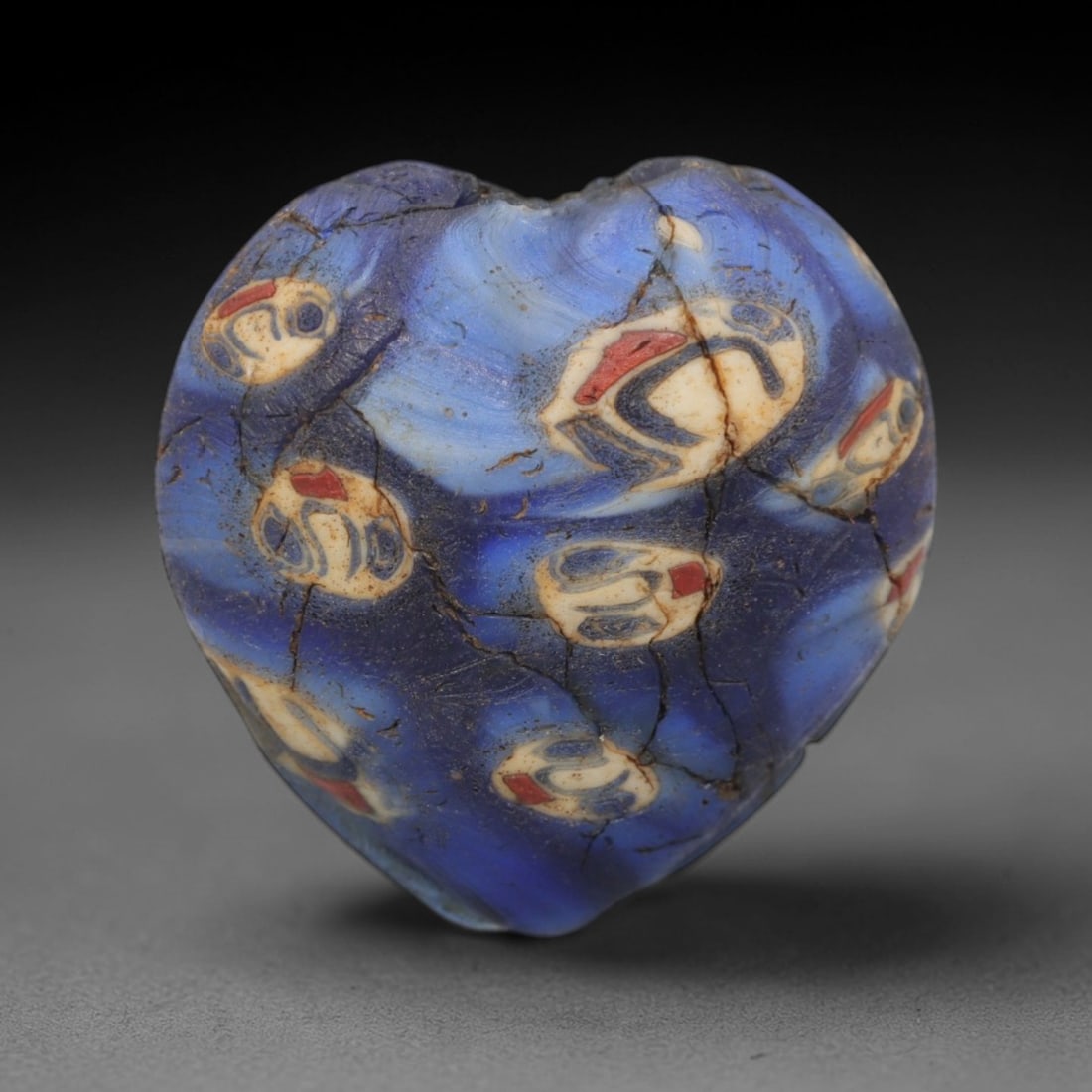 A Rare Venetian Millefiori Glass Heart Bead, 19th-20th Century, 77AD: A highly uncommon heart-shaped glass bead of Venetian Murano origin, fabricated from vibrant translucent cobalt-blue glass. The surface is decorated with scattered millefiori canes, featuring stylized