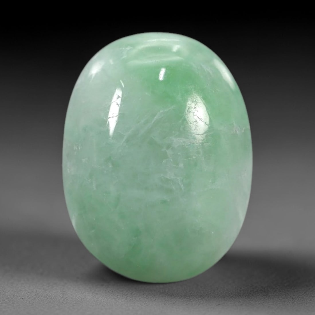4.17 Carats Apple Green Burmese Jadeite Jade Cabochon - Natural Loose Gemstone, 55XN: This singular Burmese jadeite jade cabochon presents a luminous apple green hue, soft and luminous with a translucent quality that allows light to filter gently through its smooth, domed surface. The