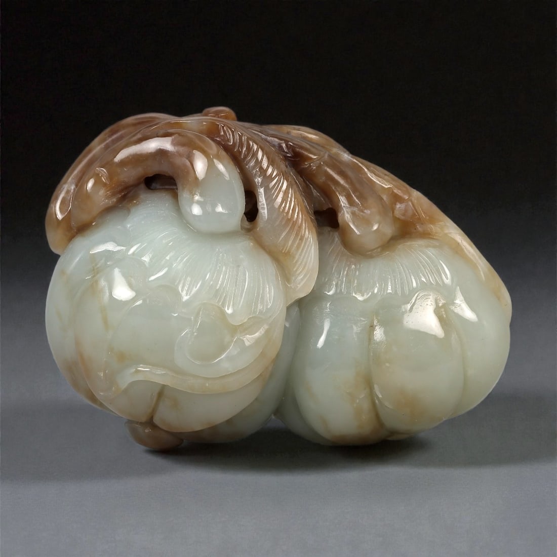 A Chinese Nephrite Jade Fruit Group, 20th Century, 21YB: Carved from pale celadon nephrite jade of Hetian type with areas of warm brown russet inclusions, the sculpture represents a cluster of fruit carved in the round, with rounded forms articulated by sha