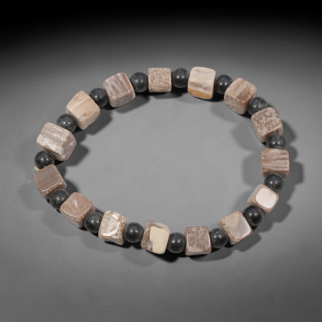 A Chinese Fossilised Wood Bead Bracelet, 20th Century, 33ZK: Strung with irregular cuboid beads of fossilised wood alternating with small spherical dark mineral spacer beads, formed into a single circular strand. The fossilised wood beads display preserved cell