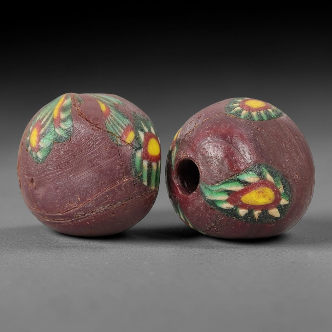 A Pair of Venetian Glass Trade Beads, 19th-20th Century, 61ZM: Formed as spherical beads, each is crafted from opaque deep reddish-purple glass with a central perforation for suspension. The surface is decorated with multiple polychrome eye motifs, each featuring