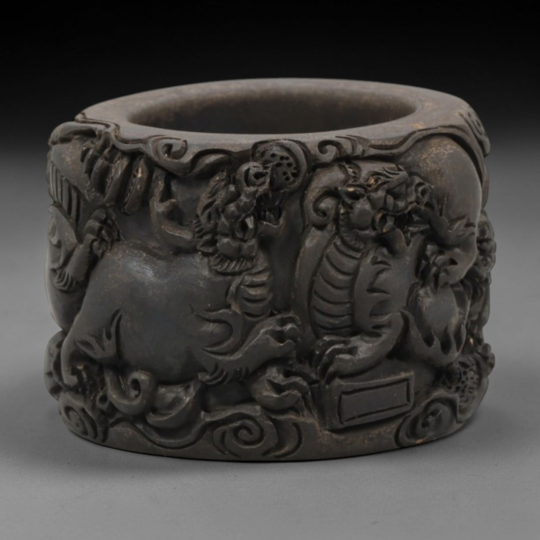 A Chinese Horn or Bone Carved Ring, 20th Century, 90FV: Carved from horn or bone with a dark, aged patina and subtle tonal variations, the ring is thick-walled and cylindrical in form. The exterior is deeply carved in high relief with multiple mythical bea