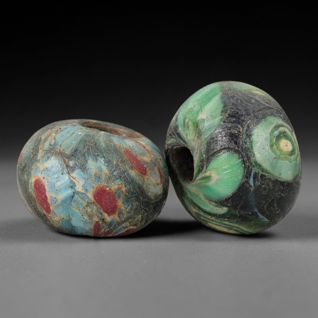 A Pair of Venetian Glass Trade Beads, 19th-20th Century, 78ZM: Formed as spherical beads, each is crafted from translucent glass with a central perforation for suspension. The surface displays marvered, swirled patterns of opaque colored inclusions, including gre