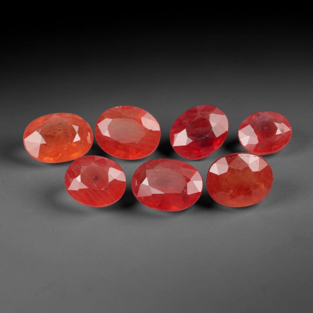 4.54 Carats Warm Orange to Red Sapphire Parcel - Natural Loose Gemstones, 99XN: This curated parcel of seven oval-cut sapphires, weighing a total of 4.54 carats with individual dimensions ranging from 4.6 to 6.1 mm, presents a rich gradient of warm hues, from bright tangerine and
