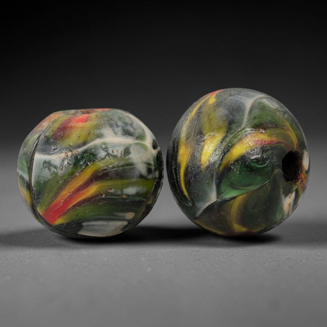 A Pair of Venetian Glass Trade Beads, 19th-20th Century, 66ZM: Formed as spherical beads, each is crafted from translucent glass with a central perforation for suspension. The surface displays marvered, swirled patterns of opaque colored inclusions, including gre