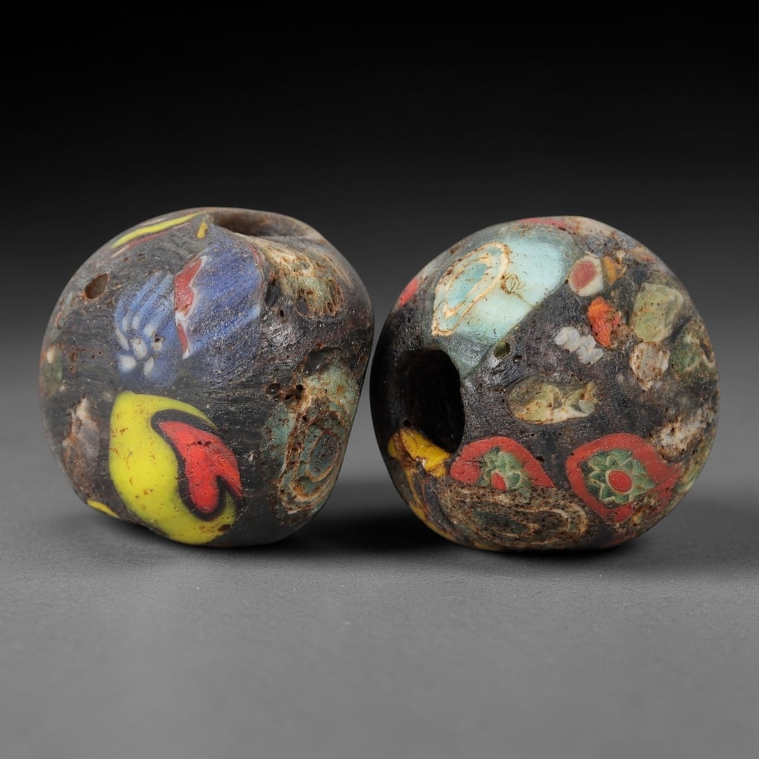A Pair of Venetian Glass Trade Beads, 19th-20th Century, 76ZM: Formed as spherical beads, each is crafted from dark translucent glass with a central perforation for suspension. The surface displays embedded, fragmented inclusions of opaque colored glass, includin