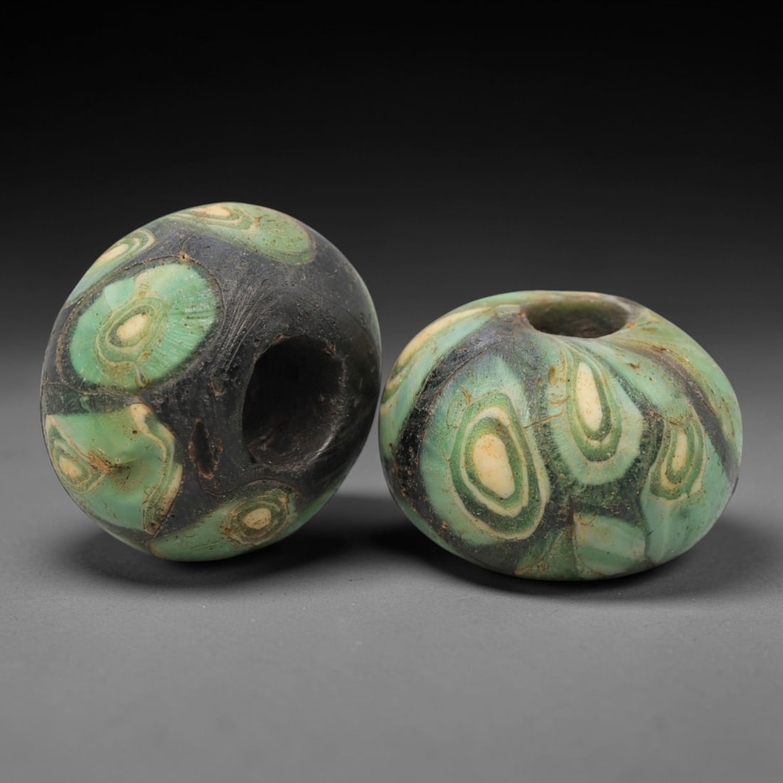 A Pair of Venetian Glass Trade Beads, 19th-20th Century, 27ZM: Formed as spherical beads, each is crafted from translucent glass with a central perforation for suspension. The surface is decorated with multiple concentric circular eye motifs, featuring green, whi